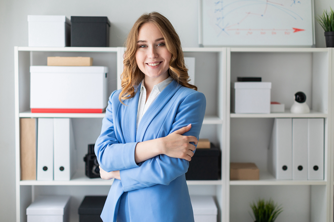 Beautiful young girl stands near a rack in the office.